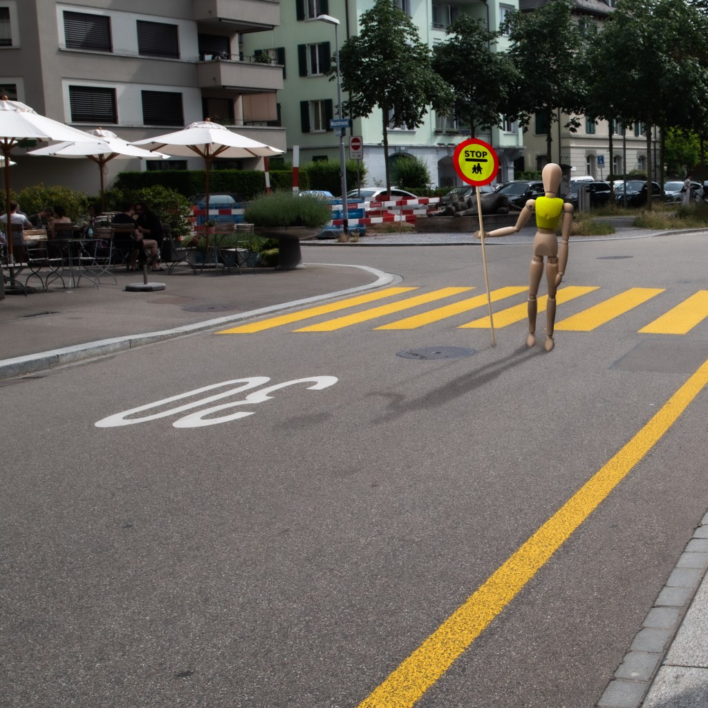 Wooden manikin holding a large "STOP / Children crossing" sign in front of a zebra crossing.