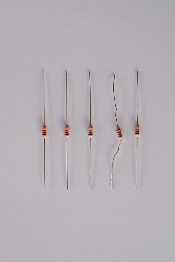 5 2.2KΩ (red-red-red-gold) resistors in a row; the fourth one is crooked, the other four are straight. The picture is dark, the paper background is visible and there's a lot of white space around the resistors.