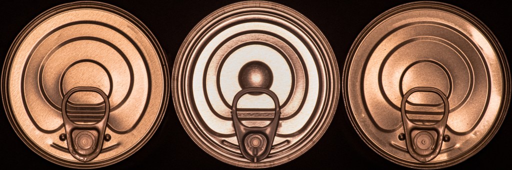 Top of three tin cans, well aligned in a row. The left and right ones are identical, the third one is of a different model.