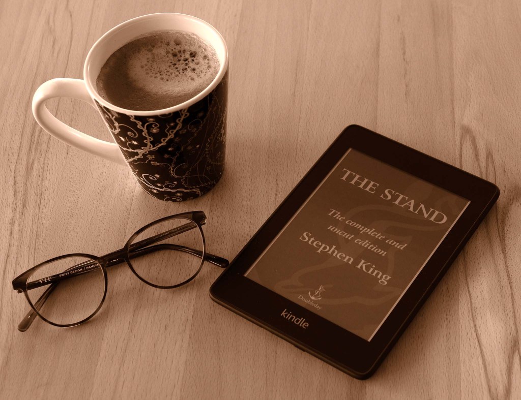 Sepia picture of a mug of coffee, reading glasses, and a Kindle showing the cover of The Stand, by Stephen King