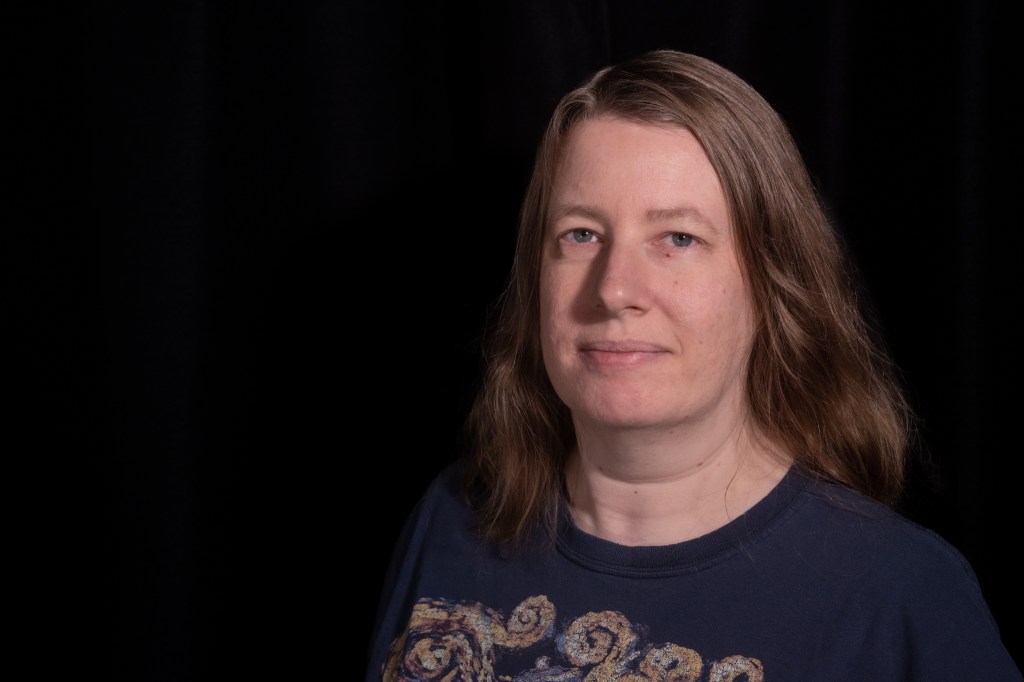 Self-portrait; a woman wearing a Doctor Who swirly t-shirt standing in front of a black background.