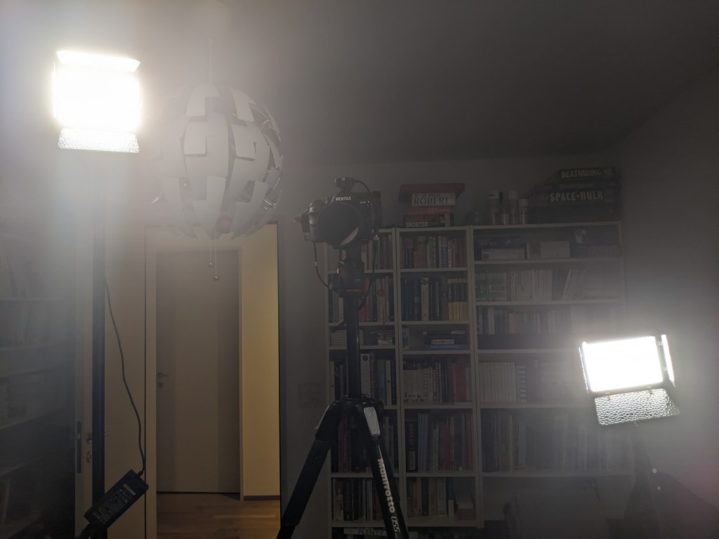 A photography setup showing a camera on a tripod, a high bright light on the left and a lower dimmer light on the right.