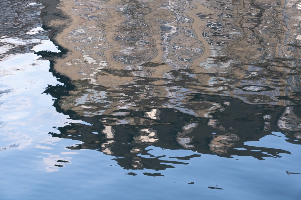 Blurry reflection of a building and blue sky in moving waters - unprocessed and somewhat unsaturated
