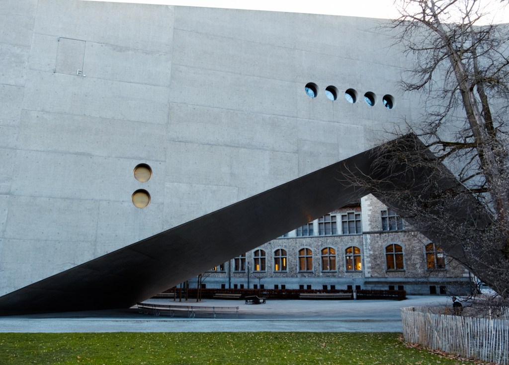A triangle in a concrete building showing a much older building behind it