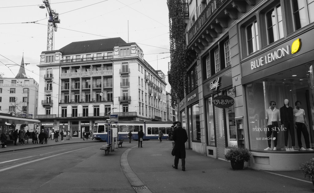 Paradeplatz in black&white; a "Blue Lemon" shop is visible at the forefront with the lemon in its logo being the first visibly colored element of the picture.