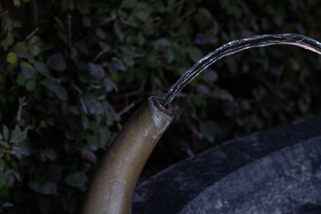 Wider, lower-exposed, unprocessed picture of the close-up of the mouth of a water fountain