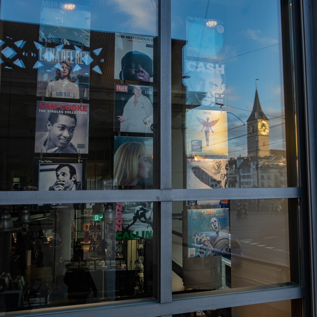 Window of a music shop displaying vinyls; the reflection of the window shows the St.-Peter church.