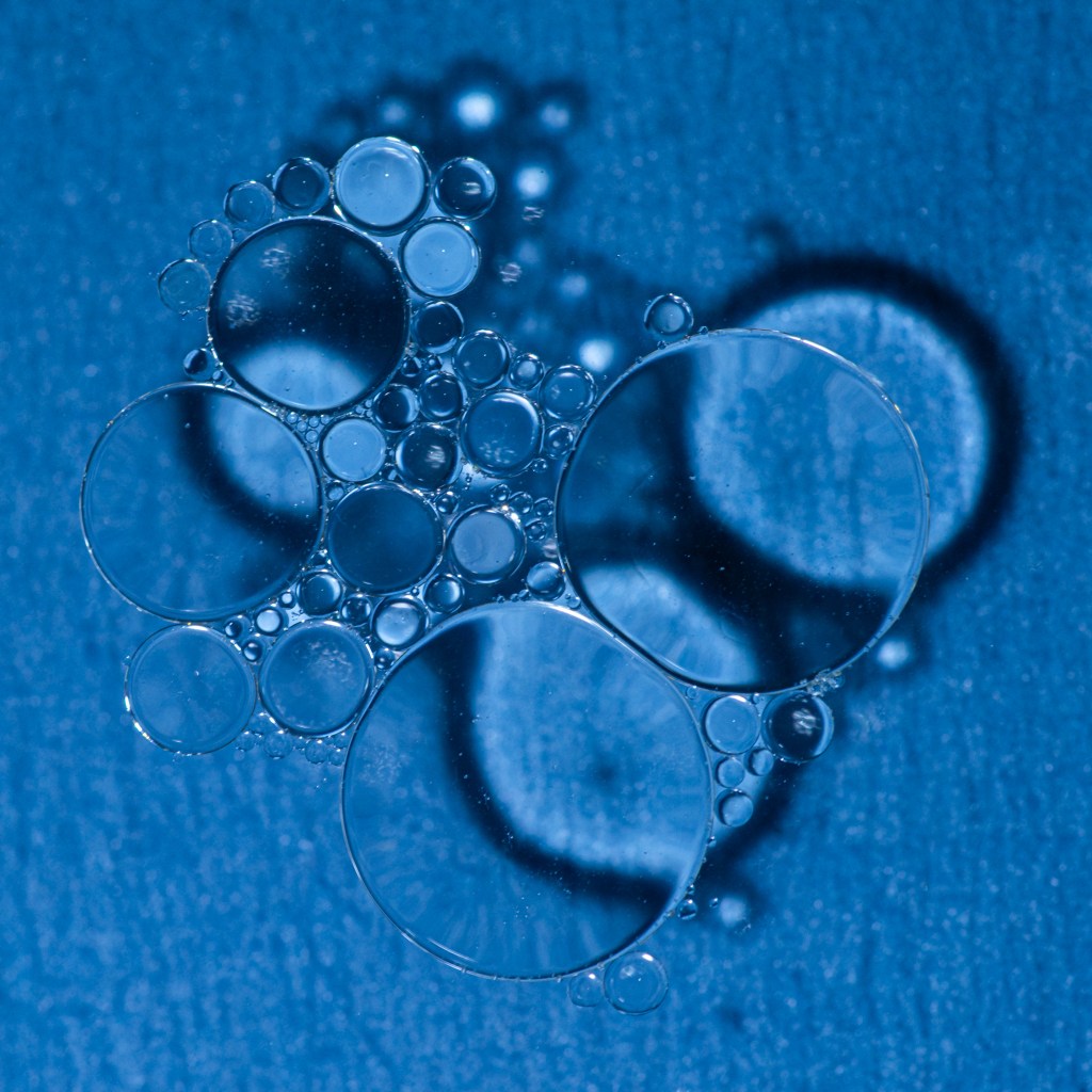 Soap bubbles structures over a blue irregular background. The shadows of the bubble structures are very visible and less sharp.