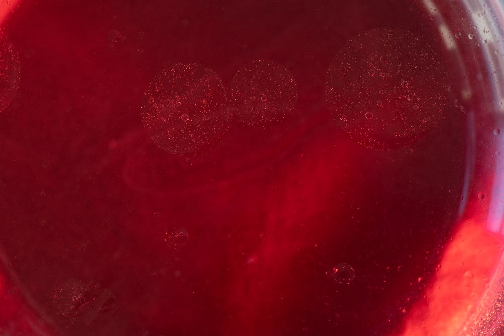 A picture of red liquid with three large oil puddles floating on top.
