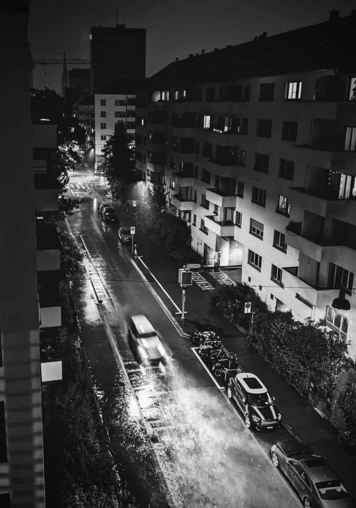 A black&white photography of a rainy night, as seen from the top of a building.