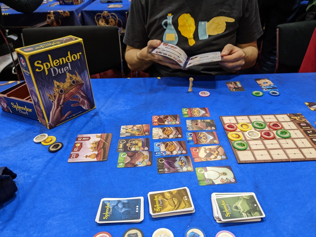 A game of Splendor Duel, showing the tableau of cards to buy and the grid of available tokens.