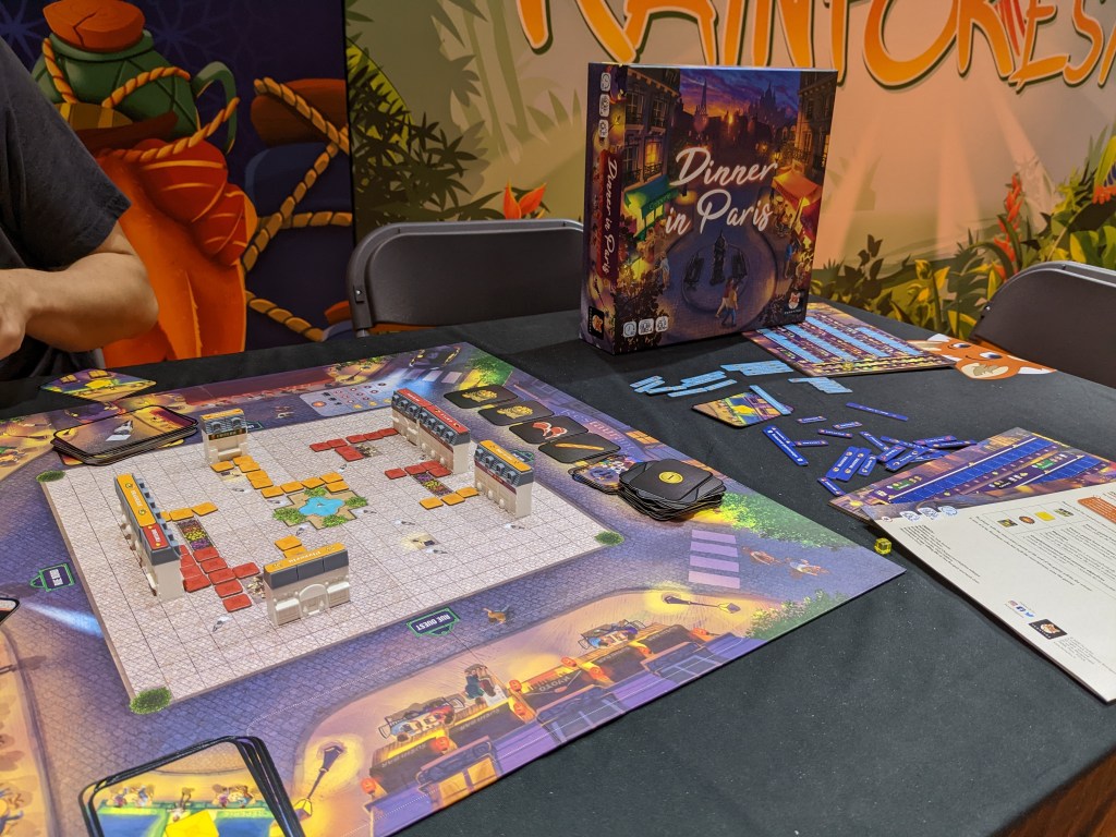A board of Dinner in Paris, representing a town square, a few restaurants on the sides of the square, and small colored tokens representing restaurant terraces.