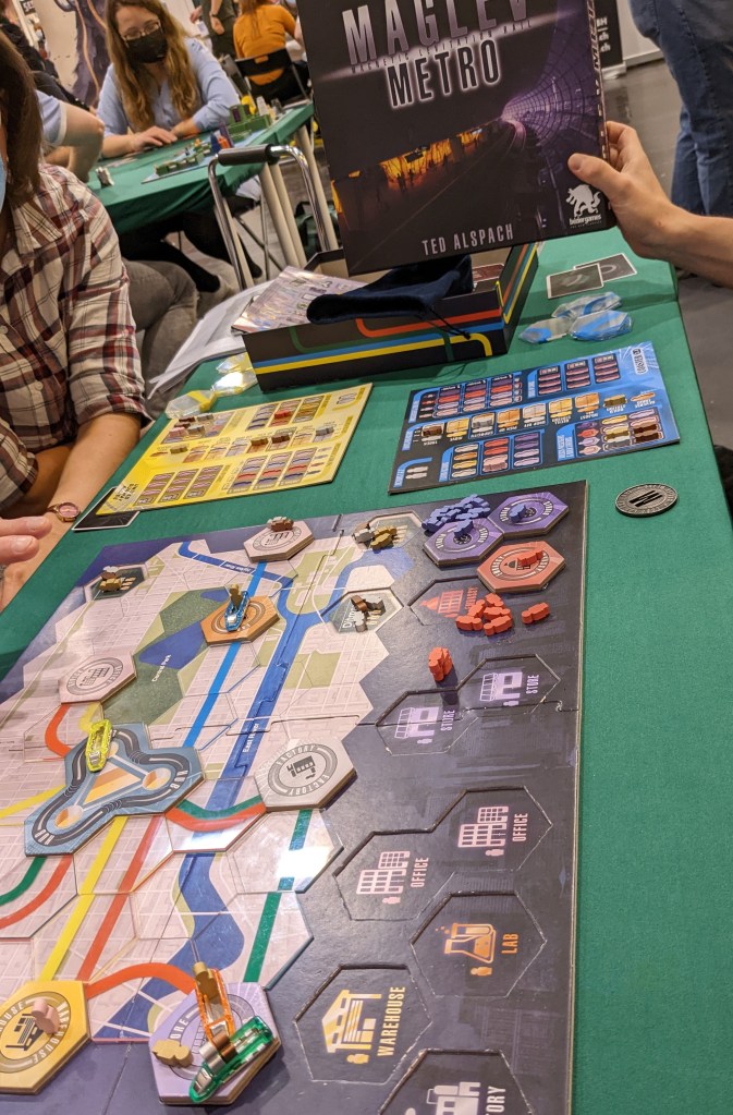 Maglev Metro: a metro map made of hexagonal tiles, where the metro lines are built with transparent tiles. In the back, player boards with actions unlocked by meeples.