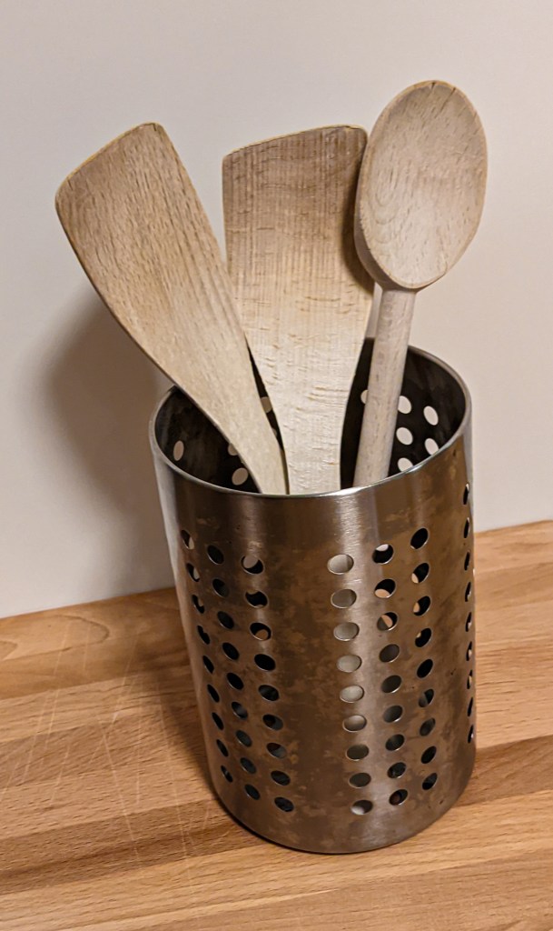 Three spatulas in a metallic pot over a wooden counter