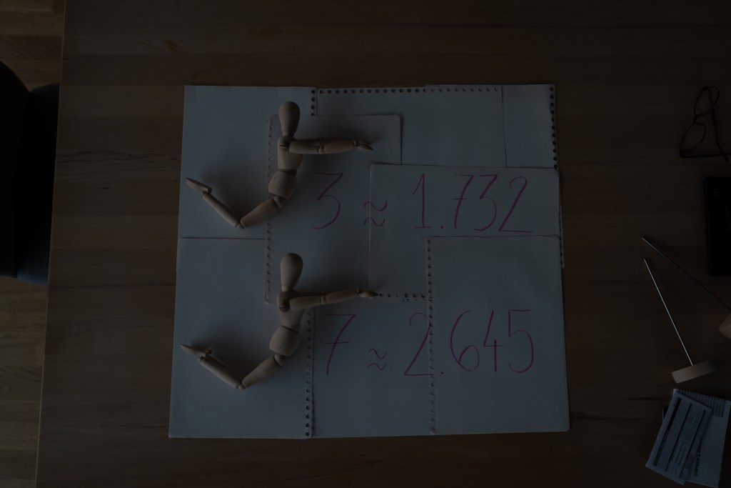 An unedited version of the previous image, showing manikins miming square root signs, uncropped and very underexposed.