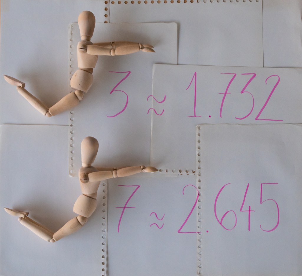 The formulas "sqrt(3) = 1.732" and "sqrt(7) = 2.645", written with pink ink on overlapping sheets of paper, and where the square root signs are not written, but mimed by wooden manikins lying on the paper.