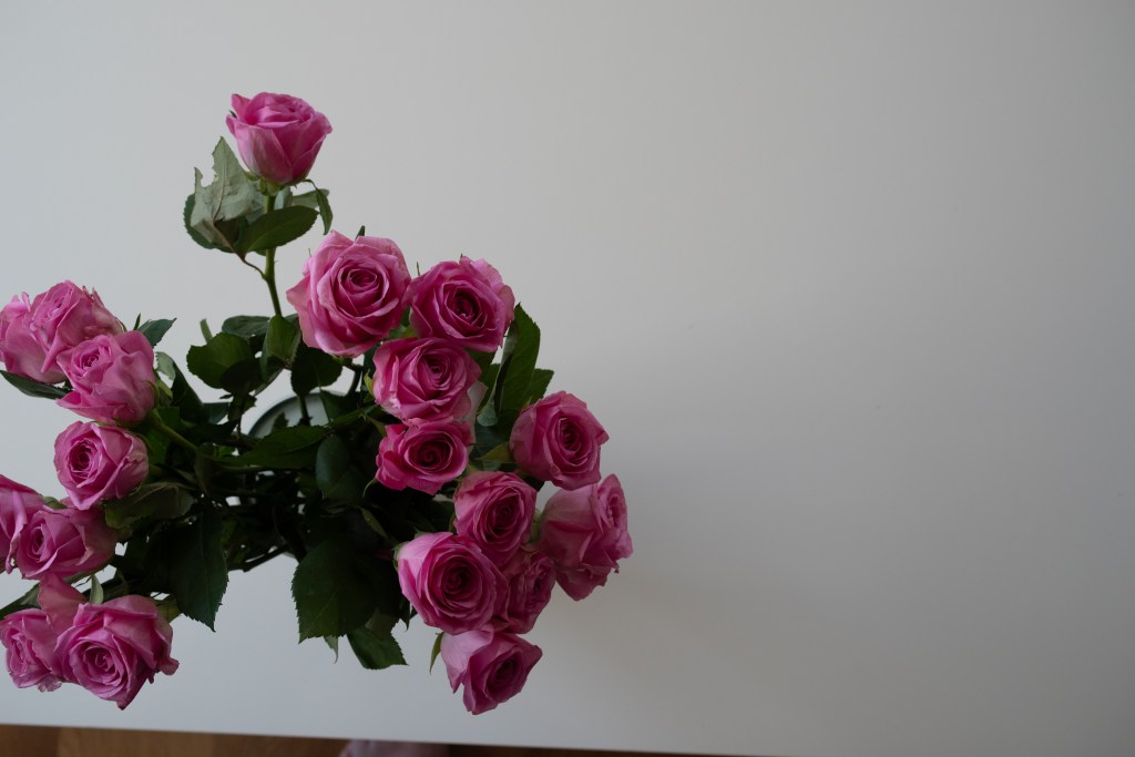 A picture of a rose bouquet on a white table, seen from above. The bottom of the table is not straight and visible. The picture is slightly underexposed.