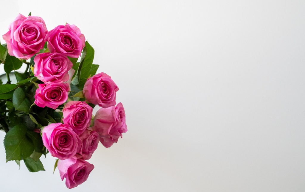 A pink rose bouquet in a vase, seen from above, with a large amount of white space on the right.
