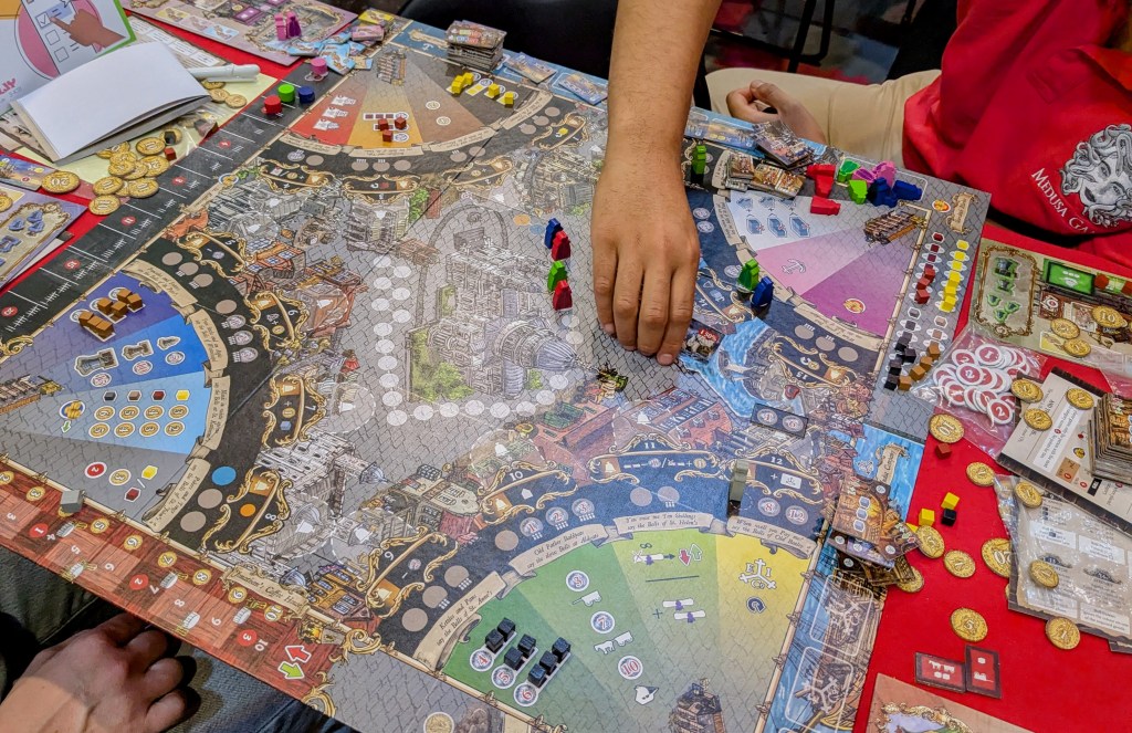 Oranges & Lemons: a large board decorated with a 18th century London theme, with round quadrants in the corners to palce meeples, and a bunch of meeples, cubes and gold tokens.