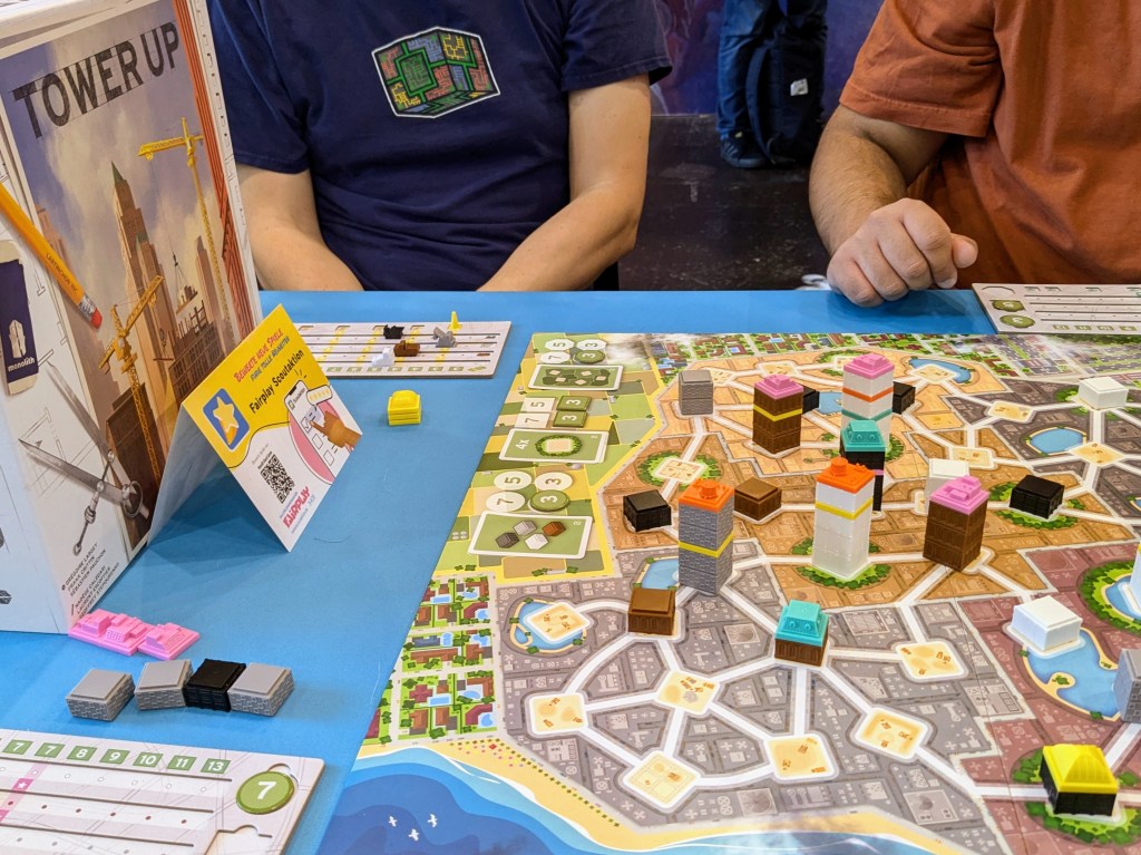 Tower Up: a board with colored districts and a network of square spaces connected by roads. Some of the spaces have stacked plastic pieces on them.