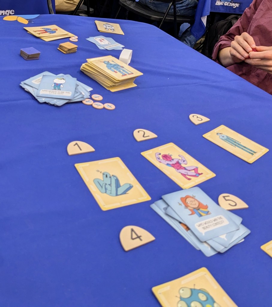 Whoforwat: cards with quirky monsters under numbered plates, as well question cards (the visible one shows "Who would win the beauty contest?"