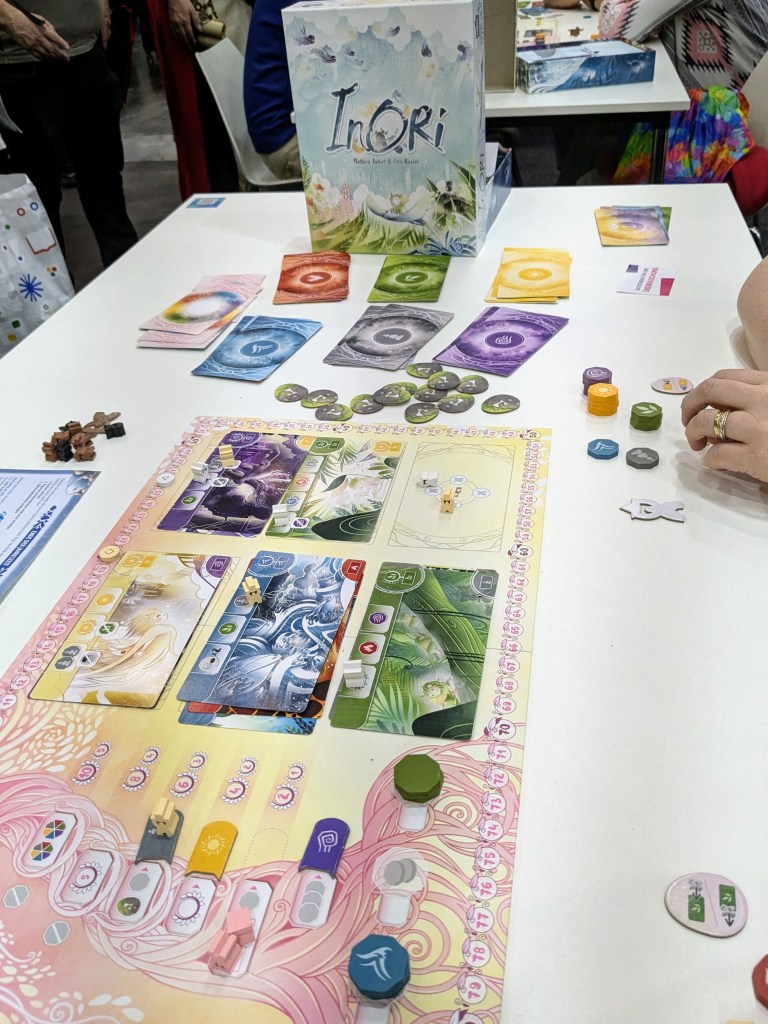 Inori: a board with a tree on the left and cards with meeples on them on the right. There's extra piles of cards and piles of tokens on the side.
