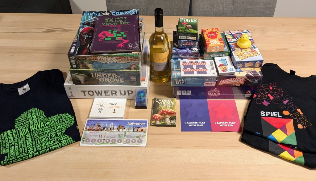 A table with board game boxes, three t-shirts, a bottle of wine and a yellow rubber duck