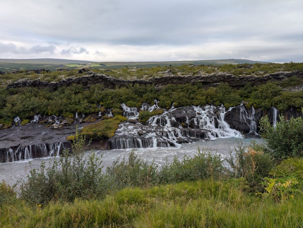A cliff with many many waterfalls spawning from the middle of it and flowing on lower levels