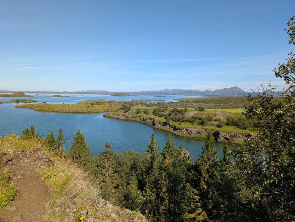 An island in the middle of very blue water, with some mountains in the far background