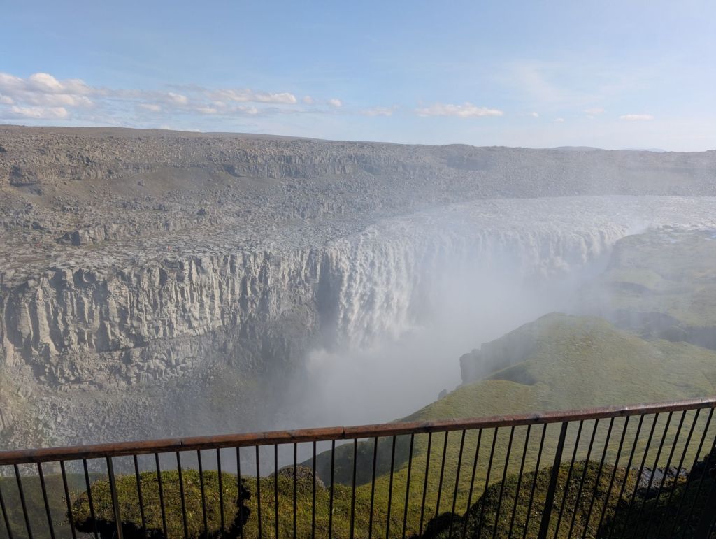 A large and powerful waterfall in front of a rock wall made of multiple vertical stripes.