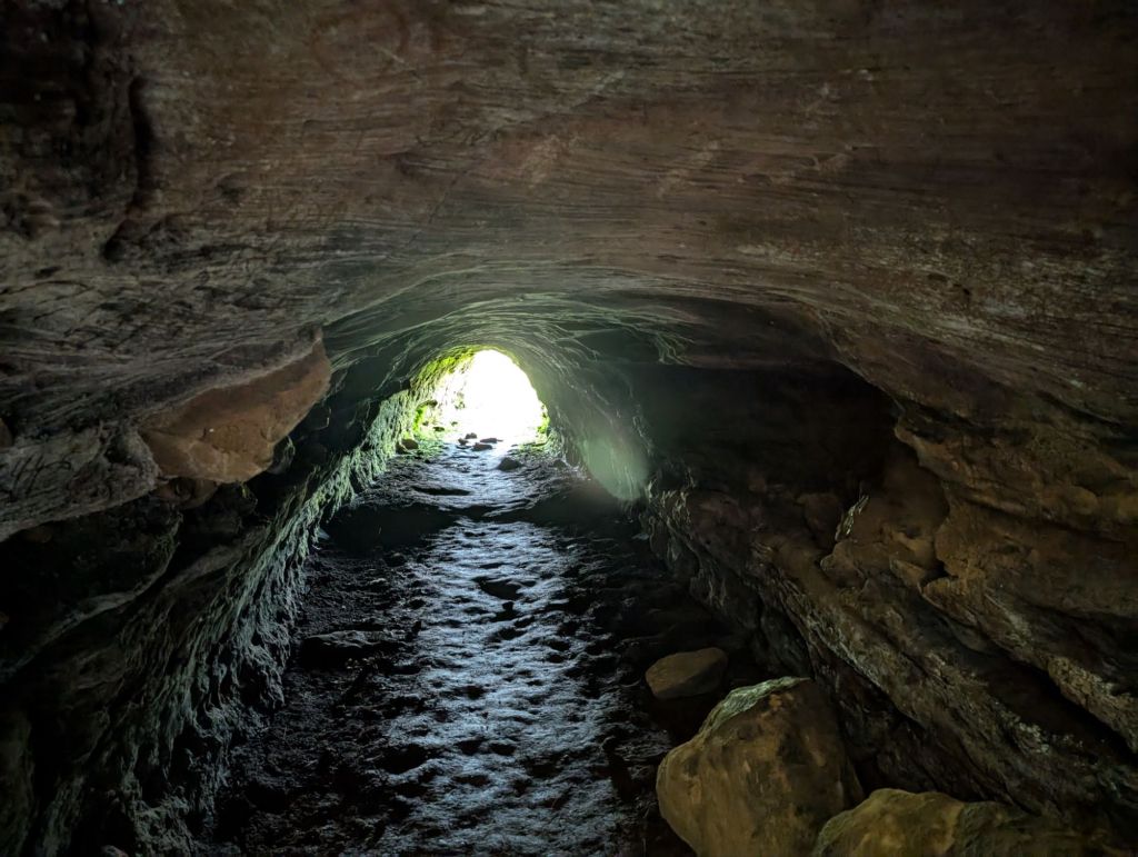 A dark tunnel dug into rocks, with the end of the tunnel providing the only light