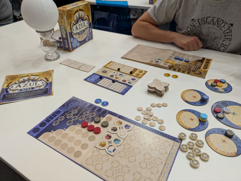 A two-player game; two boards with slots and tokens, a score board in the middle of the table, and 5 circles (four small, one large) with various colored tokens on them.