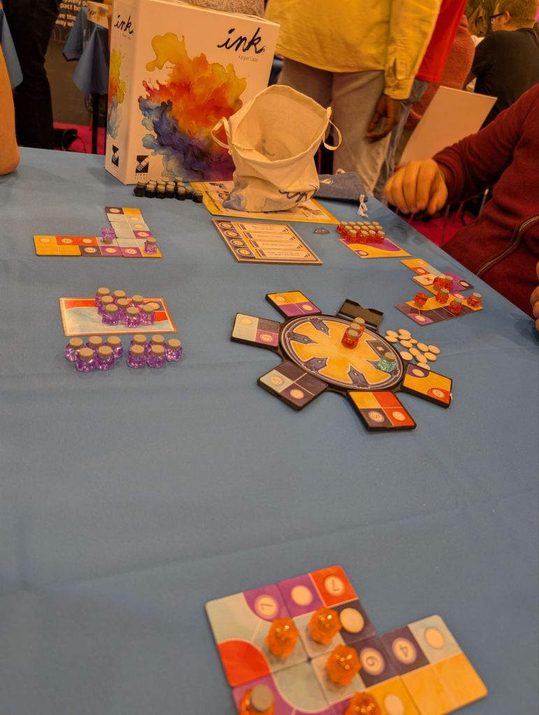 Tiles with multiple colors (purple / cyan / dark blue / yellow / red), installed in front of players; a lot of small tokens in the shape of adorable ink bottles.