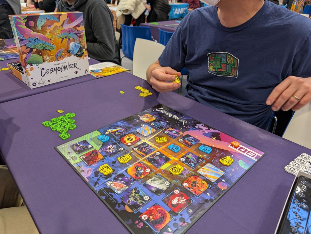 A 6x5 grid filled with colorful tiles with numbers on them, as well as yellow and blue camera tokens.