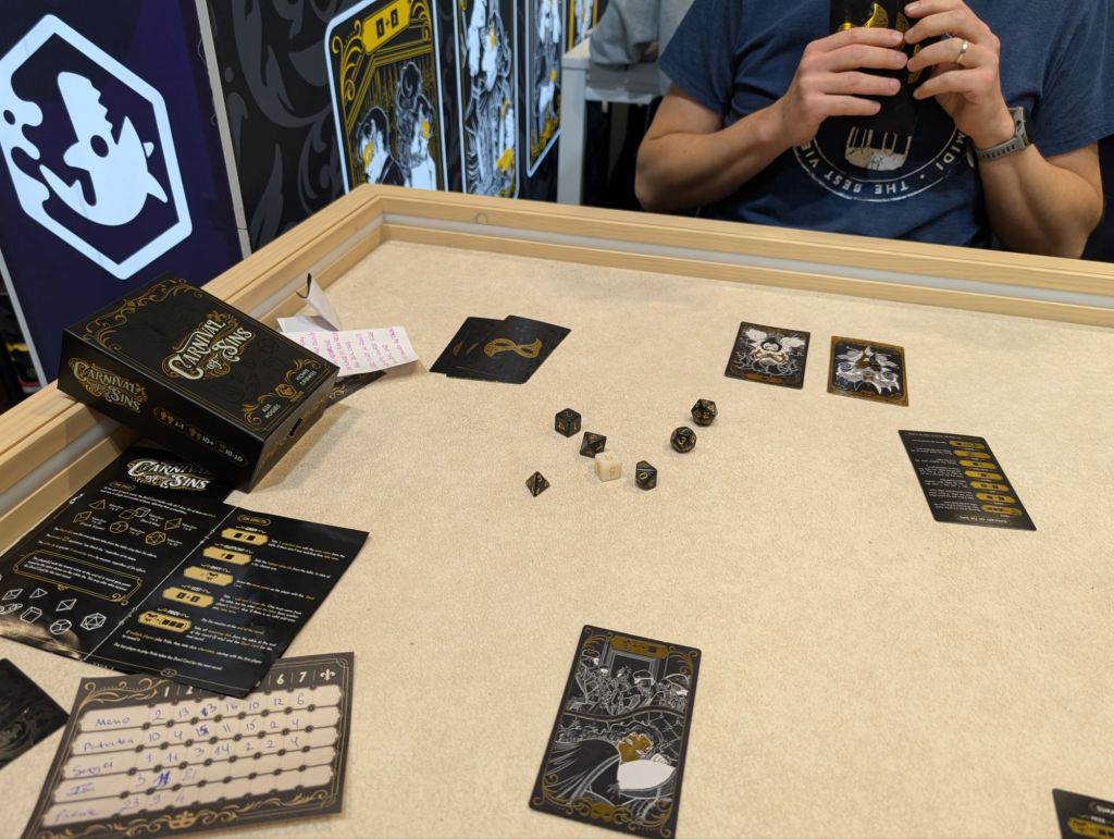 Black, white and gold playing cards showing masks on the back and sin representations on the front, and a set of black and golden dice.